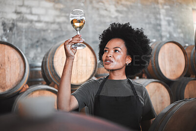 Buy stock photo Black woman tasting wine at a winery, looking and checking the color and quality of the years produce. Young African American sommelier proud of the new addition, analyzing white wine in a cellar 