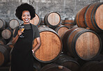 Portrait of a young woman winemaker standing with a glass next to wooden barrels of red wine in a cellar at a distillery. Entrepreneur or business owner built her business to the point of success 