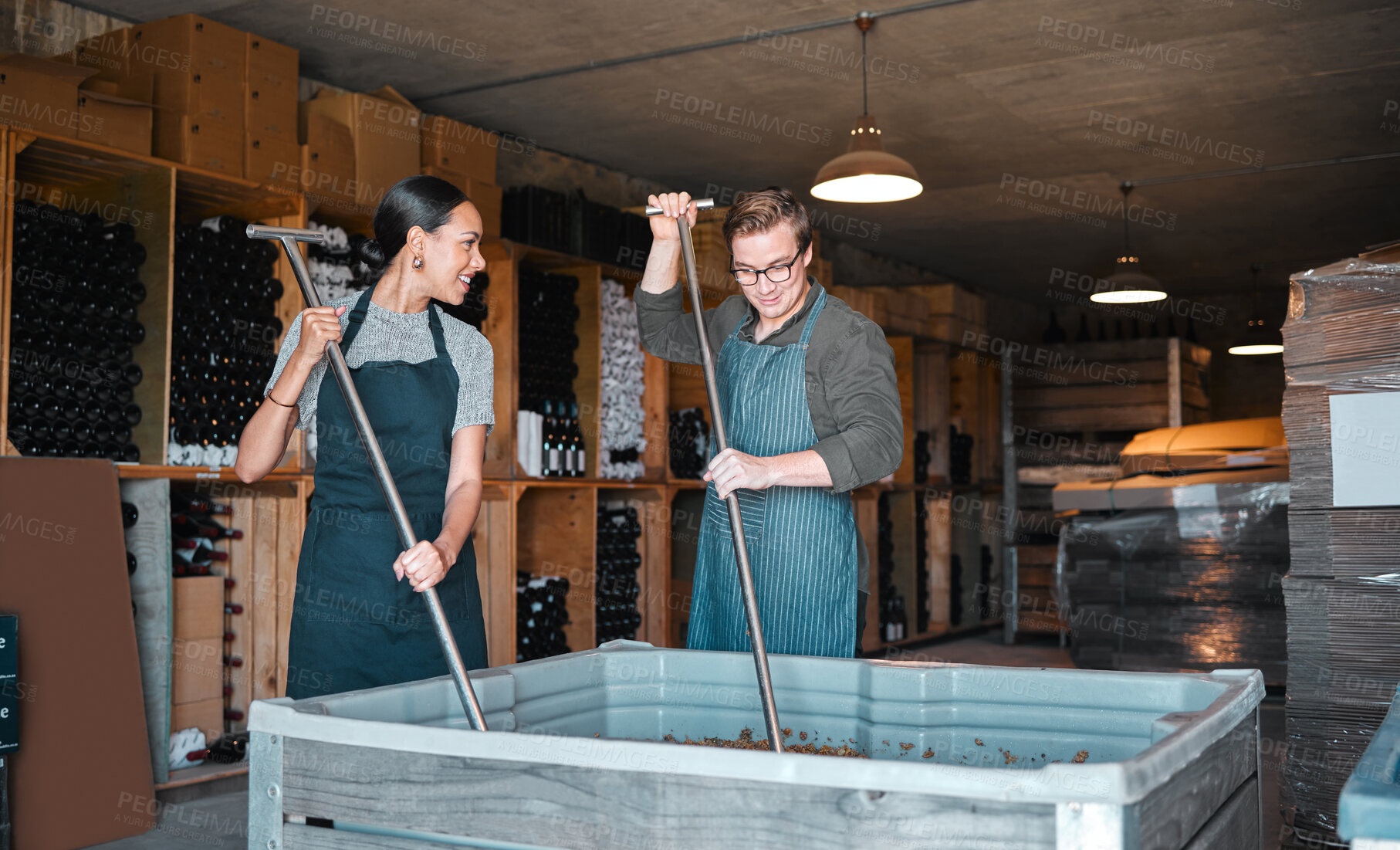 Buy stock photo Winery workers making wine with a fruit press tool or equipment in warehouse or distillery. Woman and man winemakers or factory people pressing juice of grapes manufacturing alcohol for the industry.