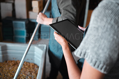 Buy stock photo Owner working on a digital tablet in a winery while a wine maker press grapes to make wine. Woman worker doing research on the internet with technology in a manufacturing distillery warehouse.