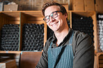 Happy, smile and proud wine, warehouse or manufacturing worker wearing glasses in a cellar with a wine collection on display. Winery manager or employee in the alcohol industry or distillery 
