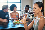 A woman drinking a glass of wine at a dinner table with friends in a restaurant and enjoying the luxury alcohol. Young African American female having fun dining with people at a celebration