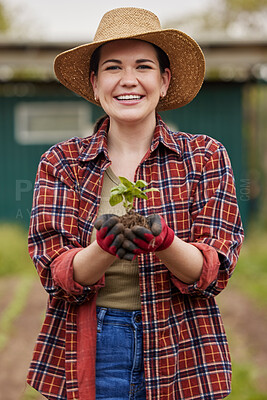 Buy stock photo Sustainable farmer holding a plant or seedling outdoors smiling and happy about her organic farm or garden. Young female nature activist that is passionate about sustainability standing on farmland