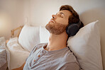 Relax. calm and resting man listening to music on his wireless headphones while relaxing on his bed at home. Relaxed male dreaming sleeping due to audiobook or podcast in his bedroom