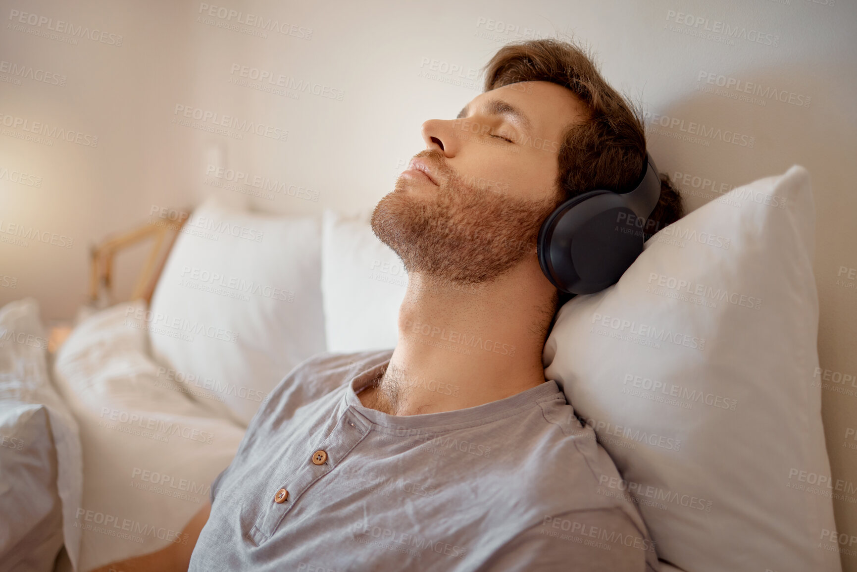 Buy stock photo Relax, meditation and resting man listening to music on his wireless headphones while relaxing on his bed at home. Relaxed and calm male dreaming sleeping due to audiobook or podcast in his bedroom
