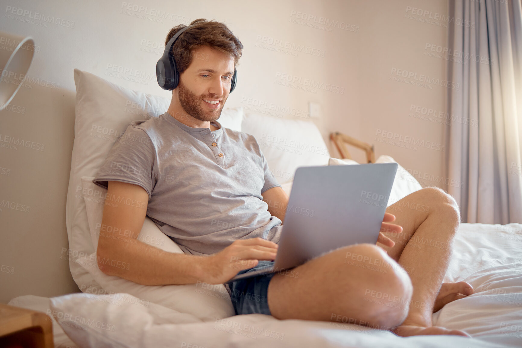Buy stock photo Relax man streaming on a laptop while listening on headphones and sitting on a bed at home. Casual male enjoying free time on weekend, watching a movie or series. Guy indoors, enjoying subscription