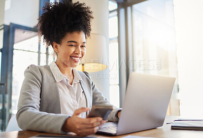 Buy stock photo Happy corporate employee texting on a phone while working on a laptop in an office, reading email. Young professional assistant multitasking to complete an online task, efficient time management