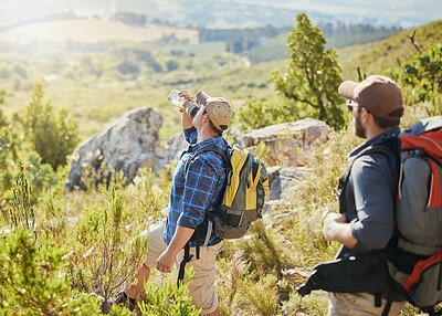 Buy stock photo Friends hiking on grass in nature for fitness, wellness and health as thirsty man drinking water and trekking in summer. Men walking, exercise and travel on rocky mountains for an adventure challenge