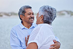 Senior, love and couple looking at each others eyes in nature at a lake or beach sand with a smile. Happy, romance and elderly man and woman enjoying environment, sea or beauty and time together.