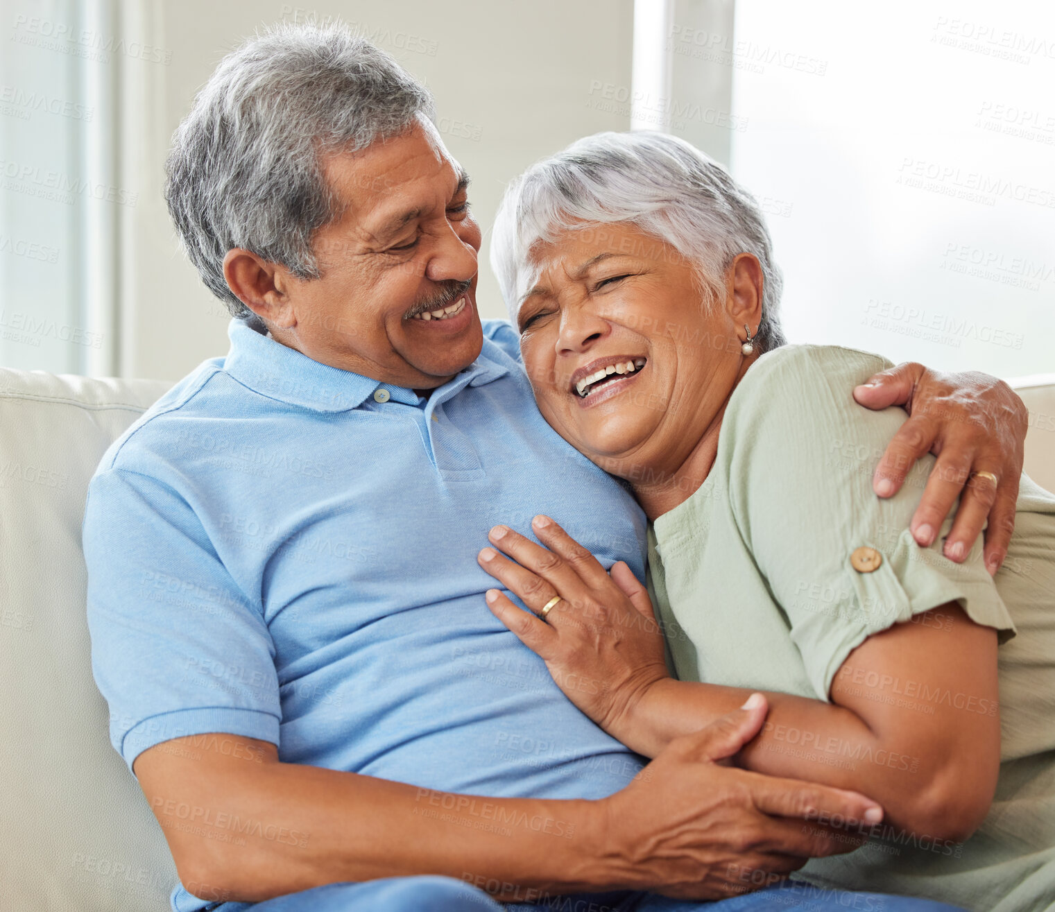 Buy stock photo Love, care and happy senior couple hugging each other while bonding and relaxing on sofa at home. Elderly man and woman sitting on a couch in the living room while embracing, talking and laughing.