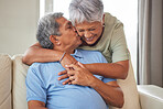 Happy senior couple kiss, hug and smile with love while relax on the sofa in the living room at home. Playful, fun man and woman laughing, smiling and enjoying retirement life together in their house