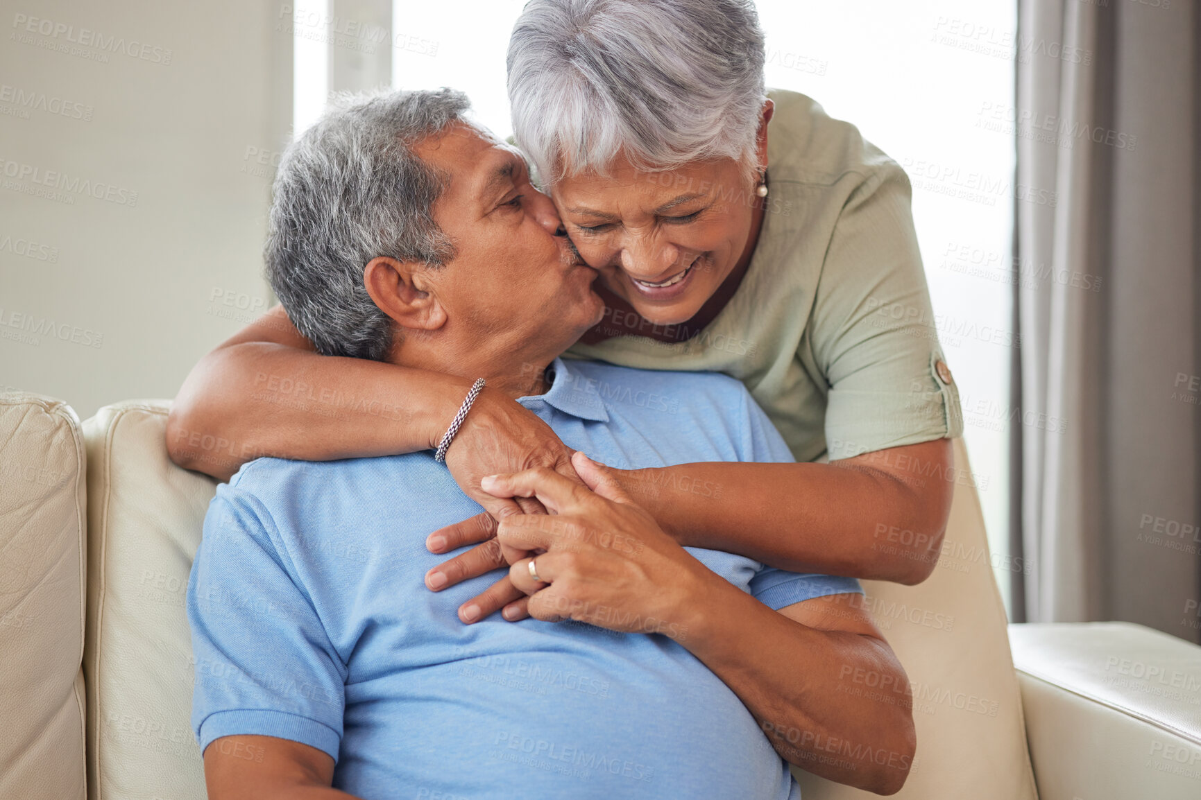 Buy stock photo Happy senior couple kiss, hug and smile with love while relax on the sofa in the living room at home. Playful, fun man and woman laughing, smiling and enjoying retirement life together in their house