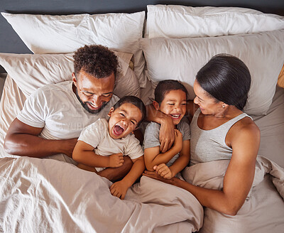 Buy stock photo Happy family bonding in bed together, playing and laughing while being loving and having fun. Young caring interracial parents sharing special moment of parenthood with two playful boys in bedroom