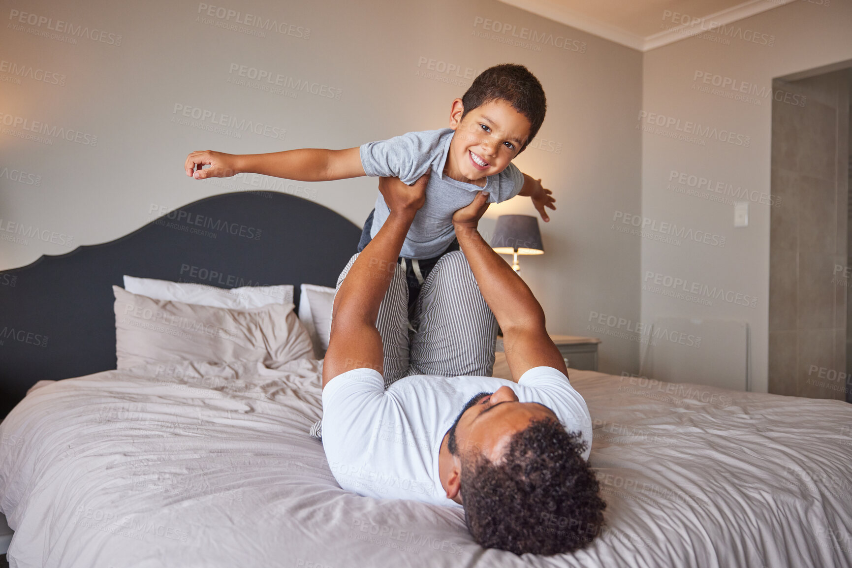 Buy stock photo Smile, love and happy father and son family time playing in bedroom bed lifting him like airplane or superhero. Loving dad, man or single parent bonding with cheerful kid in the morning at home.