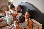 Children, bed and happy family bonding in a bedroom, having fun while hug and playing together. Interracial parents embracing their boys, enjoying a lazy morning indoors and sharing playful moment