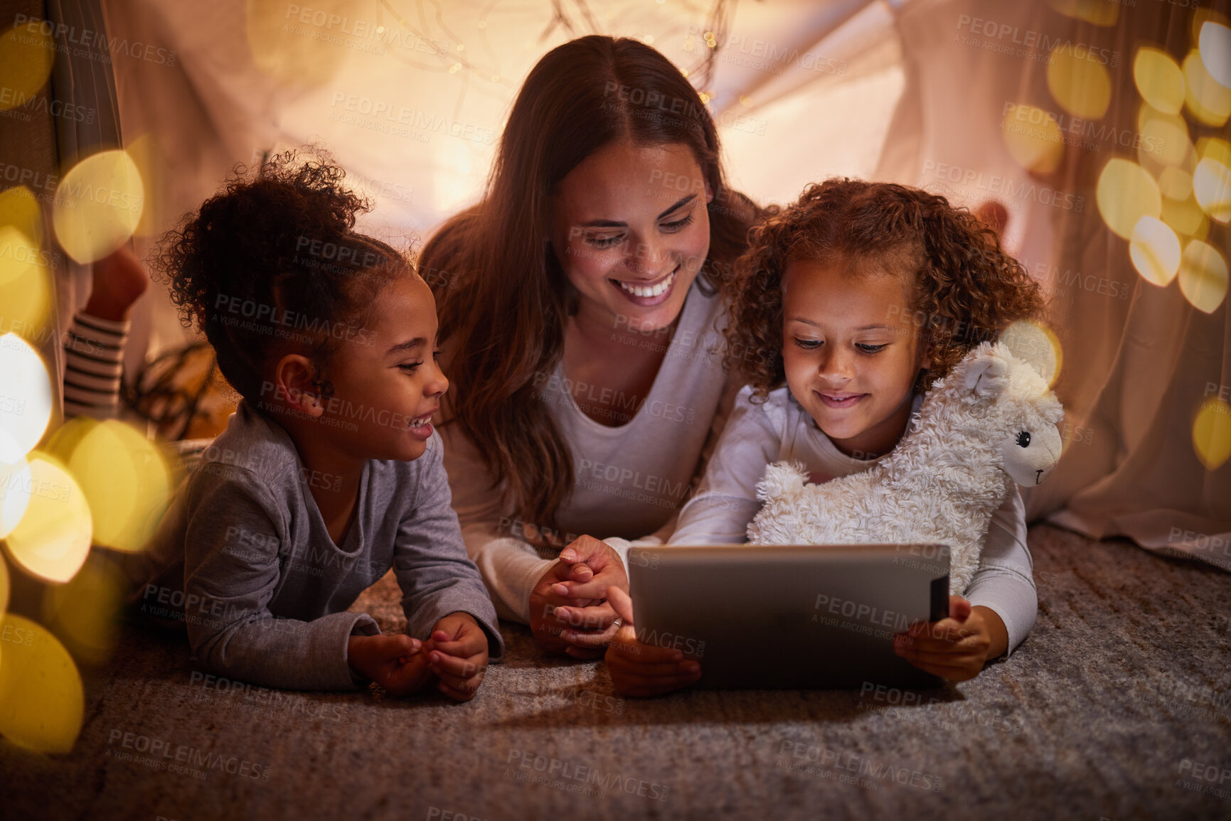 Buy stock photo Mother and children live streaming on an app using a tablet in a tent camping at home at night. Happy mom and kids watching online content or playing games with house wifi in the dark or evening