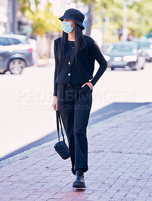 Buy stock photo City woman, on a sidewalk, with a mask on her face and  walking down the road. Urban fashion, casual walk and covid protection, life in the new normal. Calm beauty, trendy girl walks on the pavement.