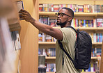 College or university student in a library taking a book from the shelf to read and study for education. Reading, learning and academic black man nerd at a bookstore to buy a textbook