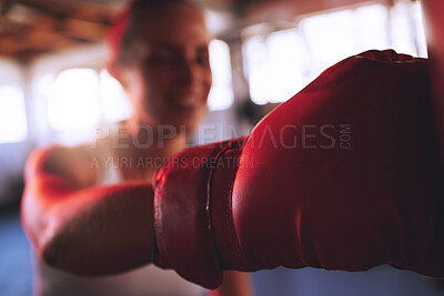 Boxing, fitness and sport with strong woman wearing boxing gloves to hit, punch and fight during training at a gym. Fit and athletic boxer female doing a workout during self defense exercise class