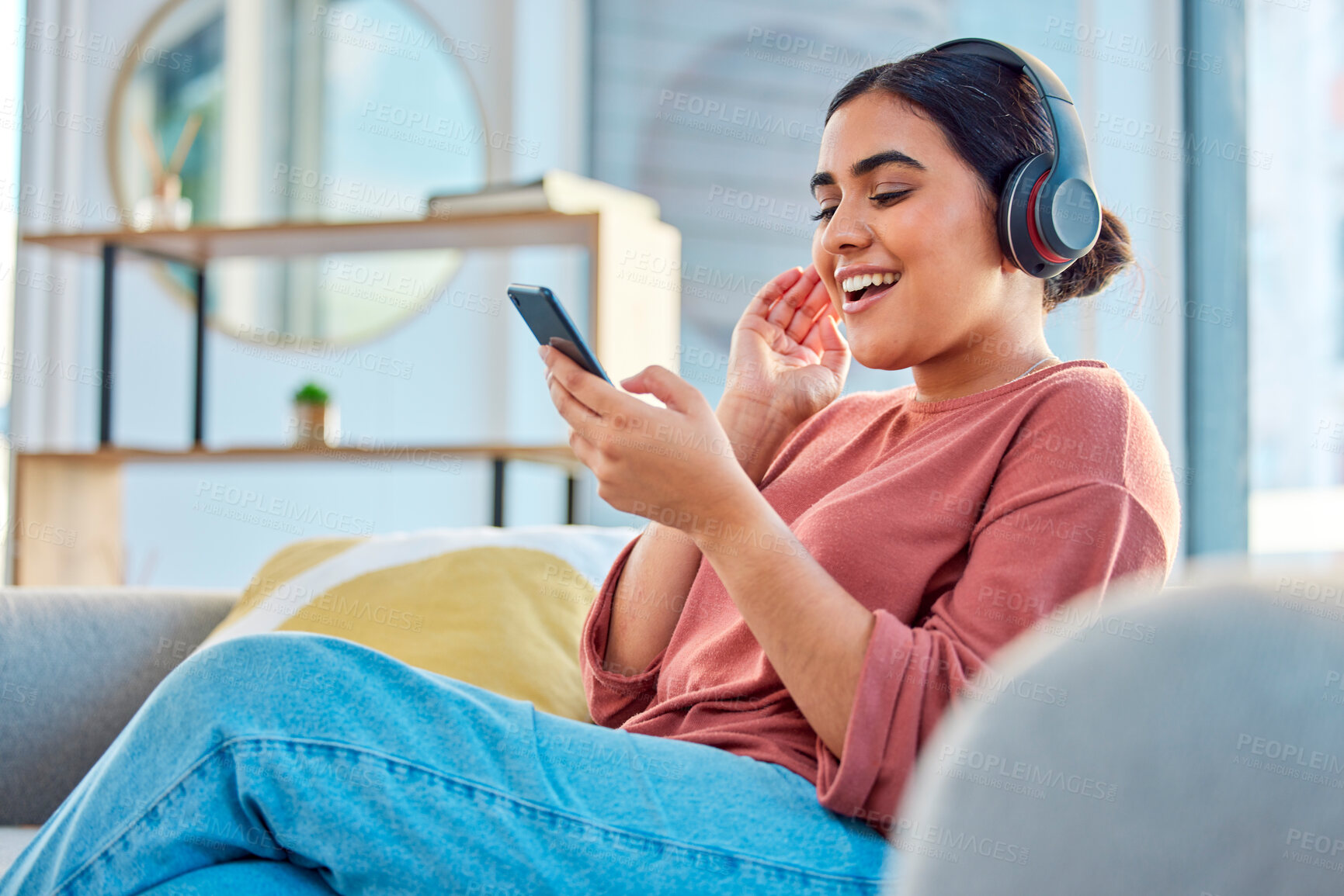 Buy stock photo Happy woman, headphones and smartphone in living room on social media app, audiobook or radio podcast on sofa. Young girl, mobile music and listening to audio, streaming and singing in home lounge