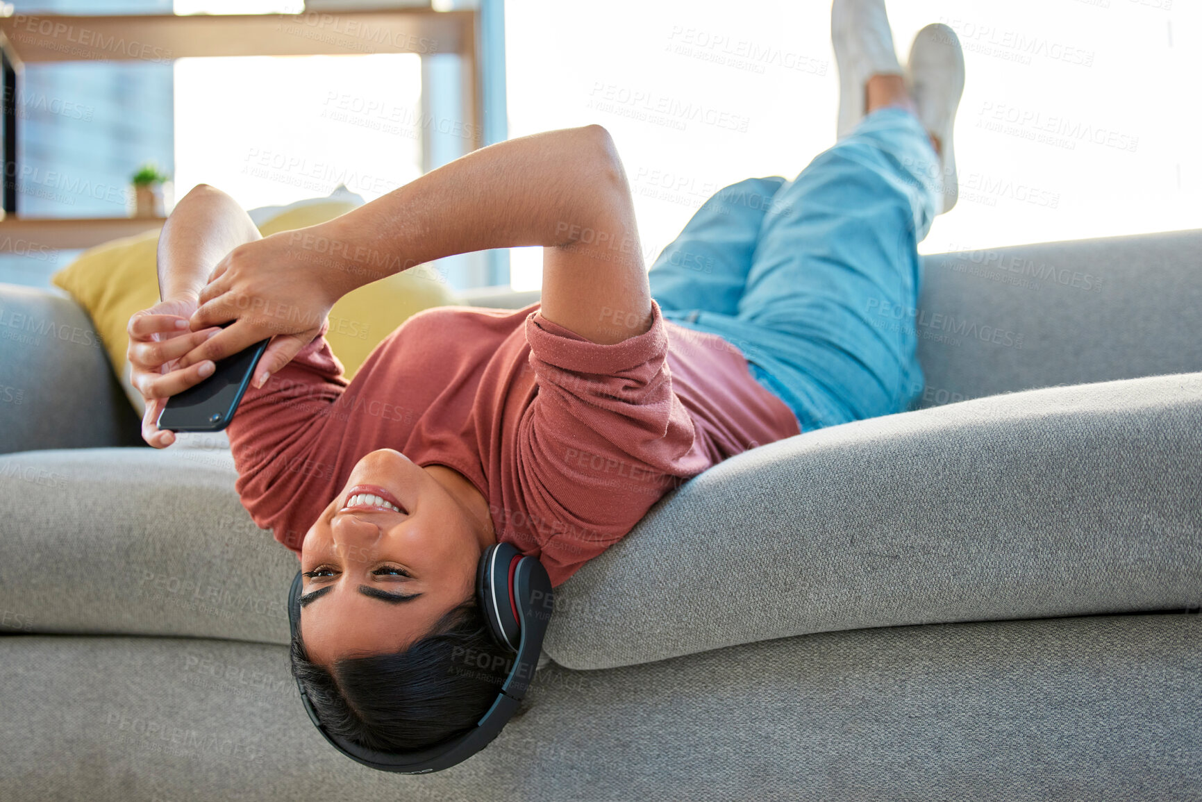 Buy stock photo Headphones, phone and woman upside down on sofa in home streaming music, radio or podcast. Relax, mobile and happy female on couch with smartphone on social media, texting or web browsing in house.