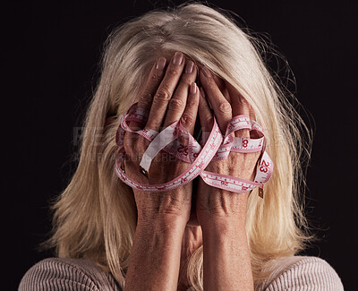 Buy stock photo Hands, tape measure and anorexia with a woman holding her face in studio on a dark background in grief. Depression, eating disorder and bulimia with a female suffering with unhealthy weight loss