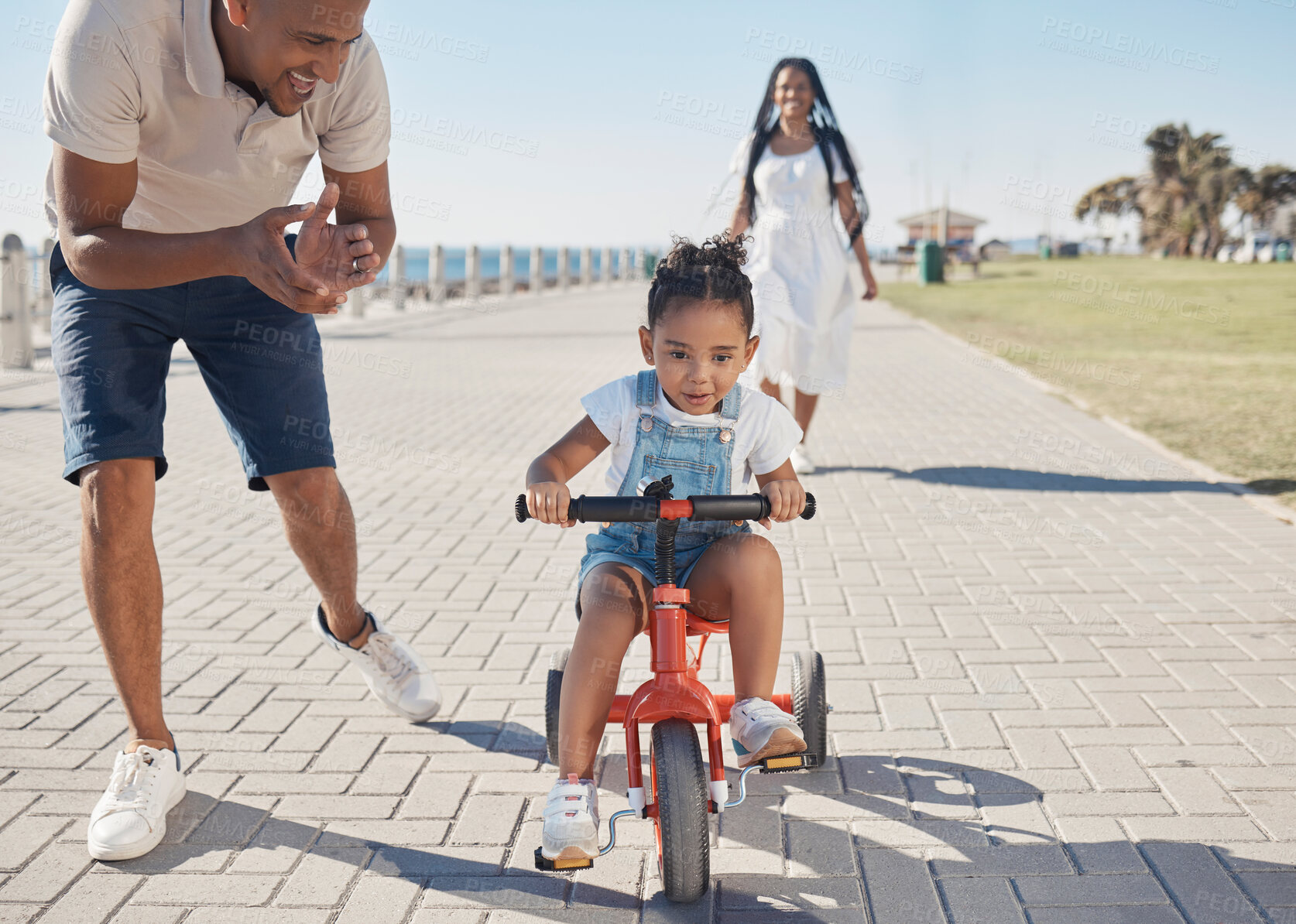 Buy stock photo Bike, learning and child with family at beach or city park for growth development, support and motivation of mother and father. Cycling girl on bicycle and african parents travel, summer and teaching