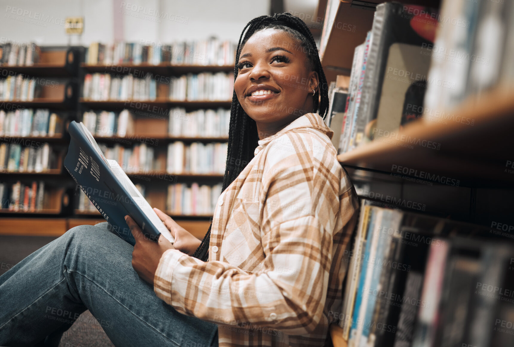 Buy stock photo University, education and black woman in library reading book. College scholarship, student and happy female learner thinking about studying, knowledge and learning while sitting by bookshelf or case