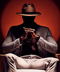 Stylish, fashionable and trendy man in silhouette sitting in a dark room with a red studio background. Edgy, mysterious and curious male mafia boss sitting in a fancy suit, hat and expensive jewelry