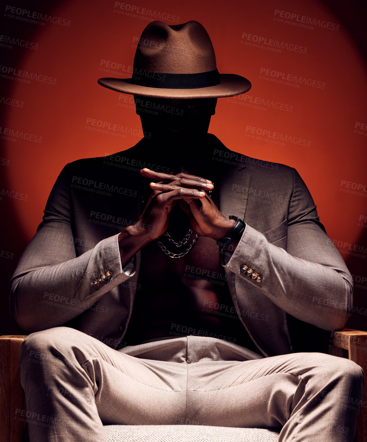 Buy stock photo Stylish, fashionable and trendy man in silhouette sitting in a dark room with a red studio background. Edgy, mysterious and curious male mafia boss sitting in a fancy suit, hat and expensive jewelry