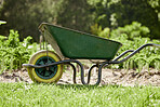 Farm or garden wheelbarrow on nature, agriculture environment or green countryside field used for farming work. Gardening equipment for lawn with sustainable grass, flower and plant growth