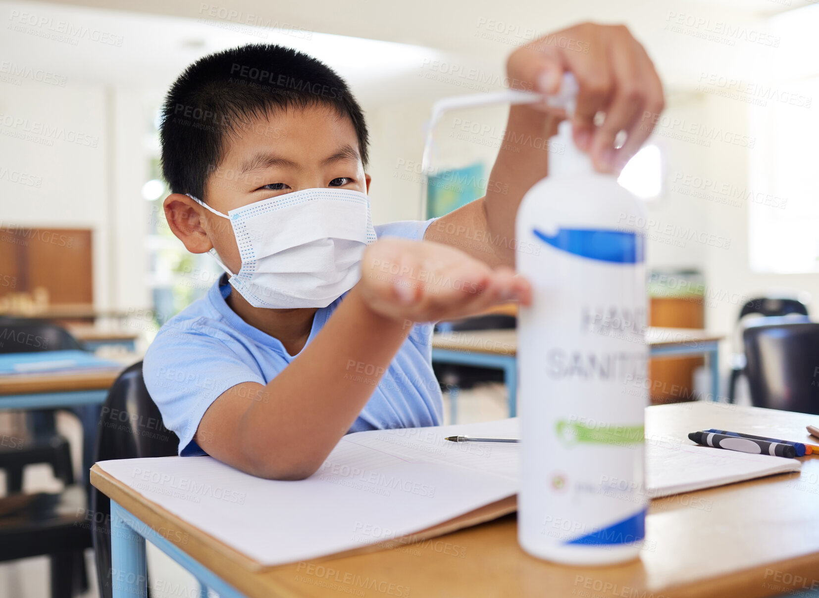 Buy stock photo Hygiene, safety and covid routine of a little boy using hand sanitizer at school. Young asian student with a mask practicing good health by cleaning his hands at his classroom desk in a pandemic