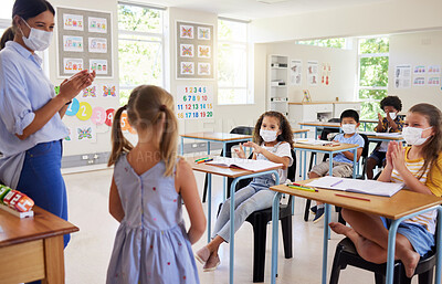 Buy stock photo Covid, education and learning with a teacher wearing a mask and clapping for a student after her oral with classmates in class during school. Young girl talking or sharing her answer in a classroom