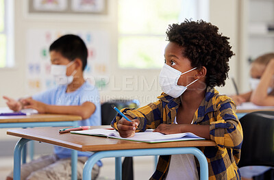 Buy stock photo Covid, education and learning with a student in class, writing and studying at a school while wearing a mask for safety. Young boy sitting in a classroom, listening to the lesson and taking notes