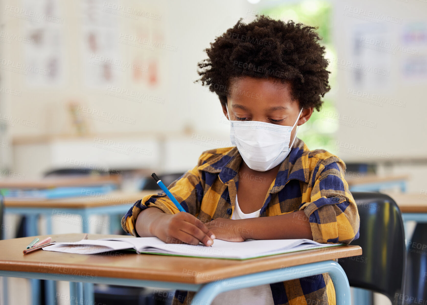 Buy stock photo School boy, student and learning while writing and working in his book inside a classroom with a mask due to covid. Young, serious and African child drawing on paper. Smart kid getting an education