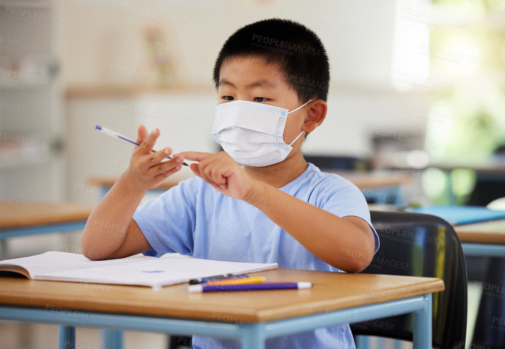 Buy stock photo Education, covid and learning with face mask on boy doing school work in classroom, writing and counting at his desk in elementary class. Asian child wearing protection to stop the spread of virus