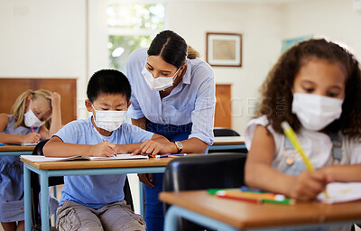 Buy stock photo Covid, education and learning with a teacher wearing a mask and helping a male student in class during school. Young boy studying in a classroom with help from an educator while sitting at his desk