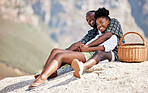 Black couple, picnic and love with a smile on a rock with South Africa blurred mountain background. Relax, man and woman in nature, holiday or summer vacation bonding, trust and safety together.



