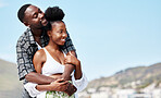 Young, love and black couple on beach hug while bonding together in blue sky seaside scenery. Happy African American people in joyful relationship embrace each other on peaceful outdoor date.