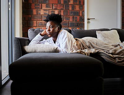 Buy stock photo Bored, depression and isolation with black woman lying on her sofa during lockdown, quarantine or pandemic. Mental health, anxiety and stress with young female thinking and looking out her window