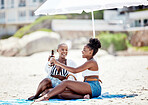 Friends relaxing and drinking a beer on the beach while on vacation together during summer. Happy black women sitting by ocean with sun umbrella talking and laughing while on holiday in south africa.