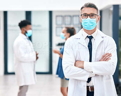 Mask, covid and medicine with a man doctor wearing a mask in a hospital for safety, health and wellness. Healthcare, medical and insurance with a male surgeon standing arms crossed in a clinic