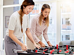 Happy employee playing table soccer, laughing and having office fun at their corporate job. Diverse women colleagues bonding while competing in a friendly foosball game during a break together