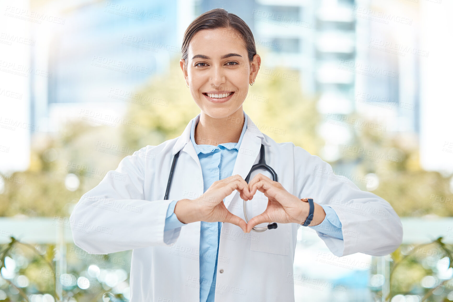 Buy stock photo Smile medical doctor with heart sign hands gesture in modern health clinic or hospital. Happy, positive and wellness young woman healthcare worker or physician with support, love and care symbol