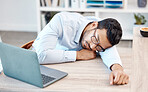 Tired, headache and sleeping worker behind laptop while lying his head on his desk in his office. Stress, burnout and chronic fatigue with young professional male feeling exhausted and overworked