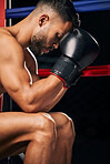 Boxing gloves, boxer sports man in fight match or tournament and prepare. Fitness, training and strong or powerful young prizefighter sitting in a ring thinking of technique, motivation or challenge