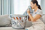 Woman on sofa smell clean laundry at home, in living room while cleaning or doing housekeeping. Lady smile on couch with washing basket in lounge, sniff fresh fabric or clothes in house.