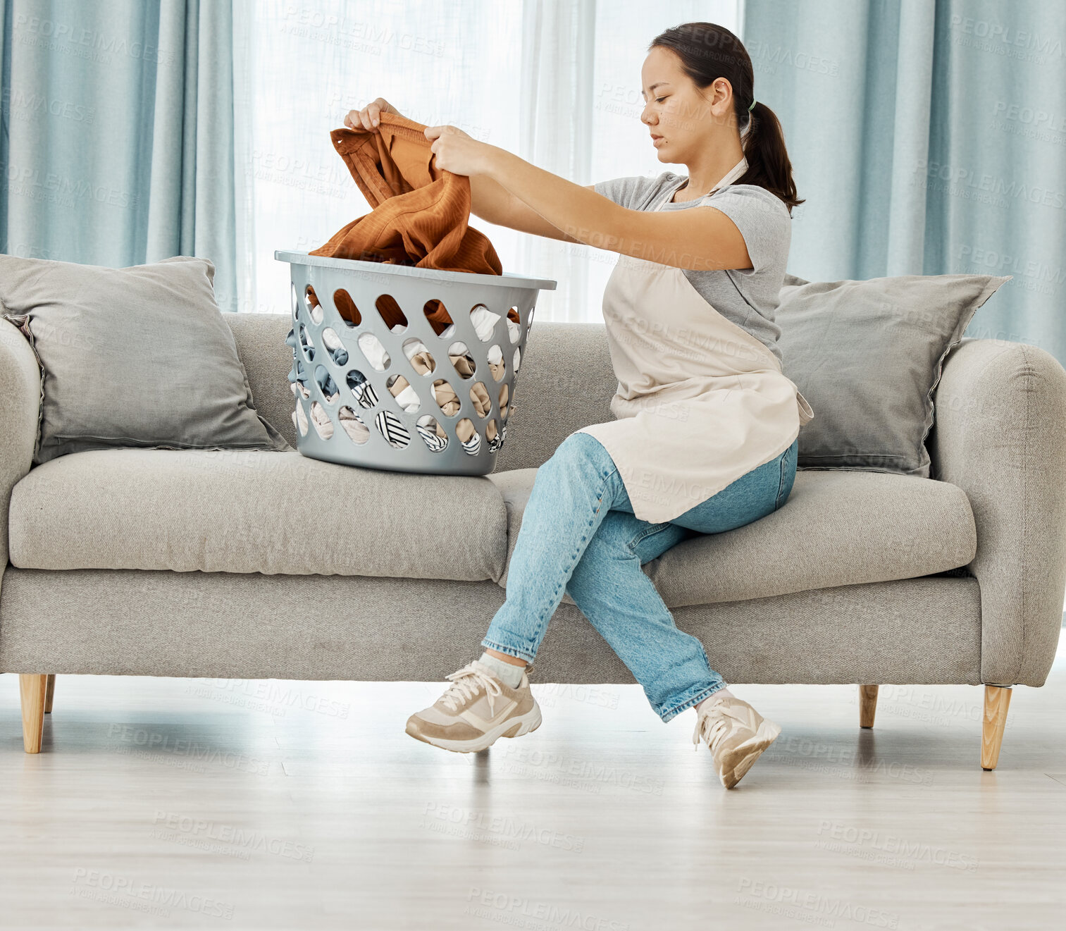 Buy stock photo Laundry, basket and cleaning with woman folding clothes on sofa of living room at home. Housekeeping, domestic and lifestyle with young maid or housewife with fresh linen, garments or washing