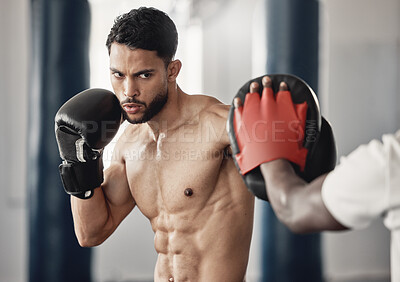Fitness, training and a man boxing in gym with personal trainer and sparring pads. Health, motivation and exercise, boxer throwing a punch. Fight, muscle and workout with sports gloves in mma studio.
