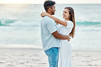 Couple love at beach, look in eyes and hug, with sunset over ocean in nature background or scene. Happy young, man and woman on sea sand smile together, sun setting over waves in backdrop or horizon.